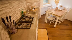 A modern kitchen with a gas stove, sink, and wooden flooring. There is a dining table with chairs and a vase with dried plants.