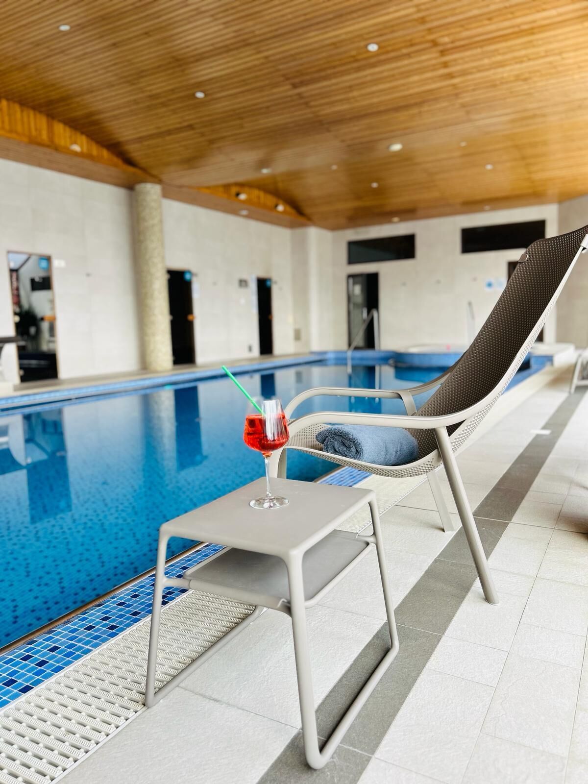Ett avslappningsområde vid poolen med en pool, en solstol och ett bord med en drink på.