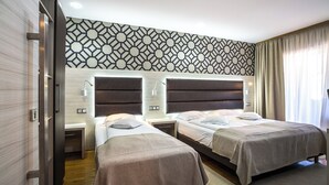 A hotel room with two beds, a patterned wall, and a window with curtains.