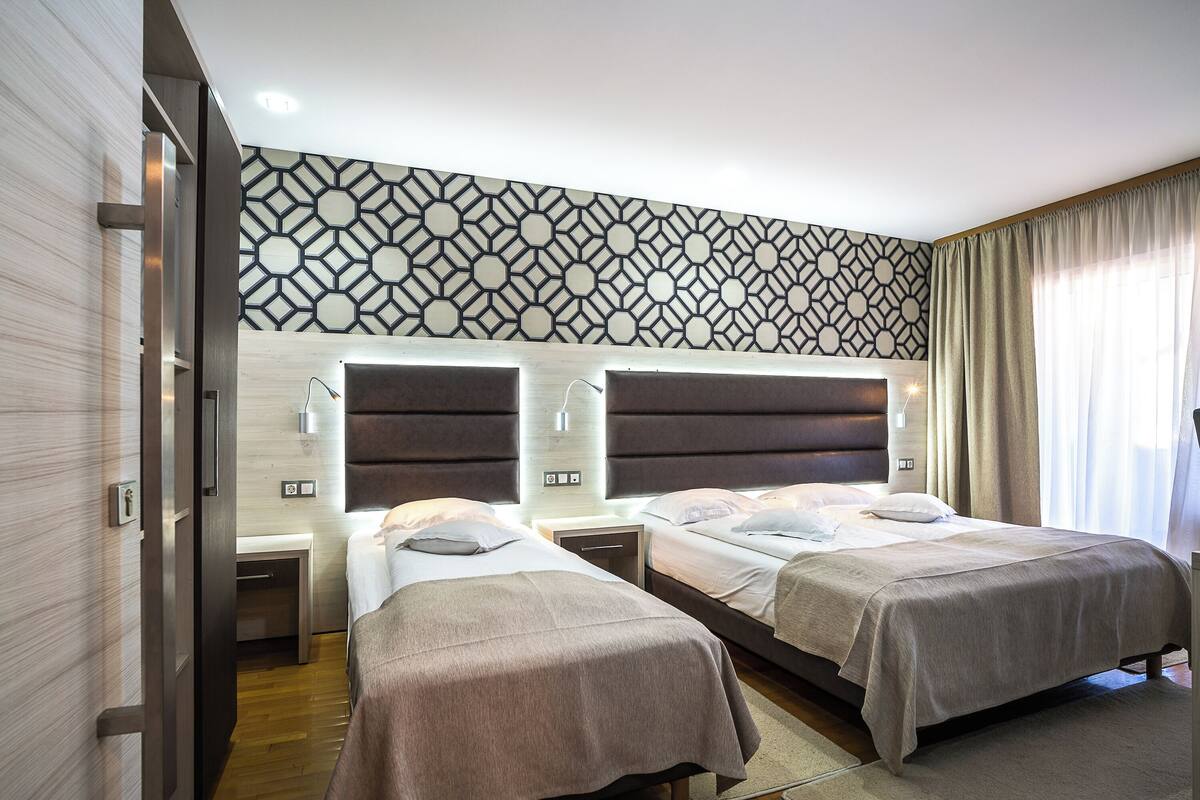 A hotel room with two beds, a patterned wall, and a window with curtains.