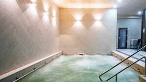 A spa room with a wooden ceiling, a green floor, and a small seating area with chairs and a table.