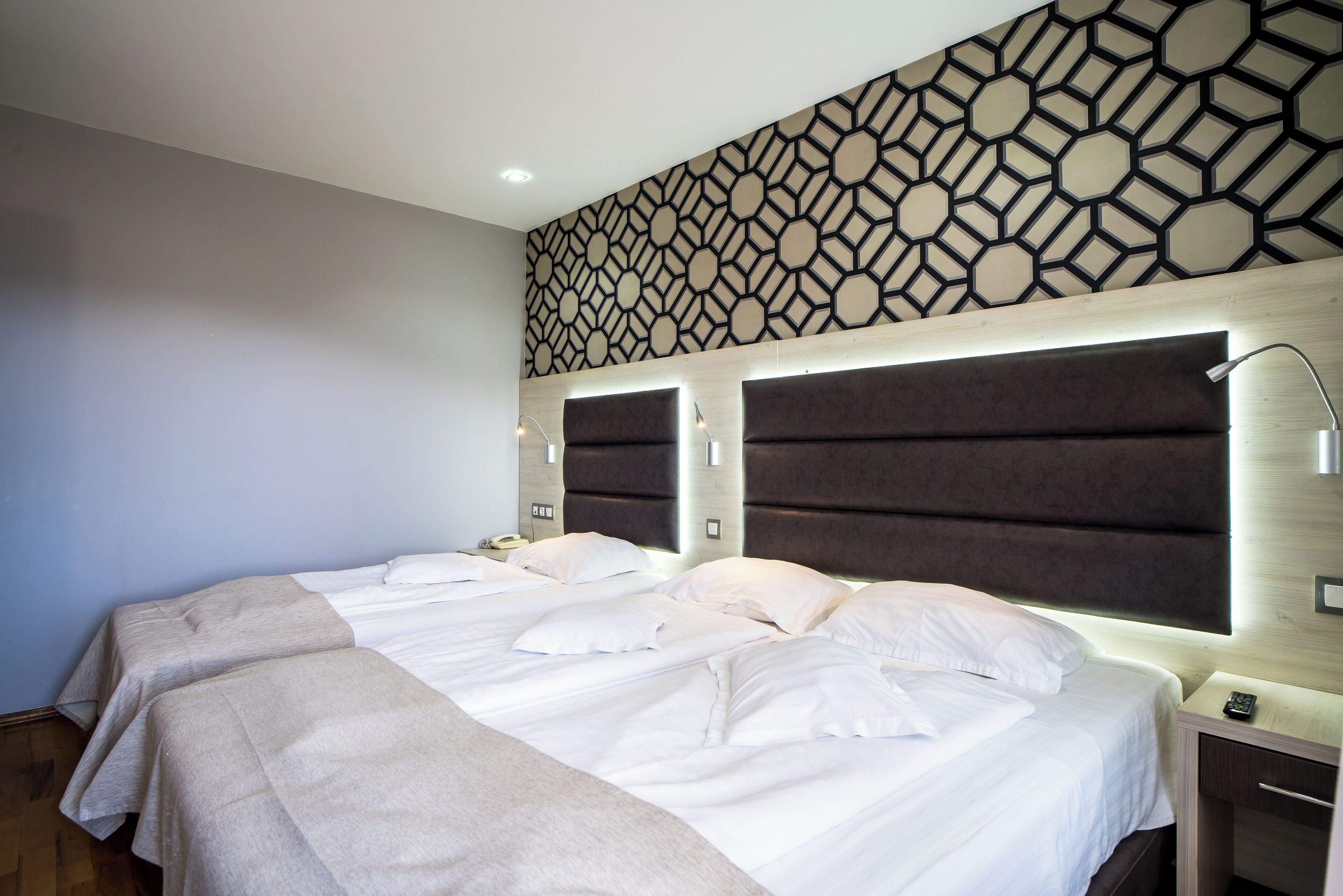 A hotel room with two beds, a patterned wall, and a bedside table with a lamp.