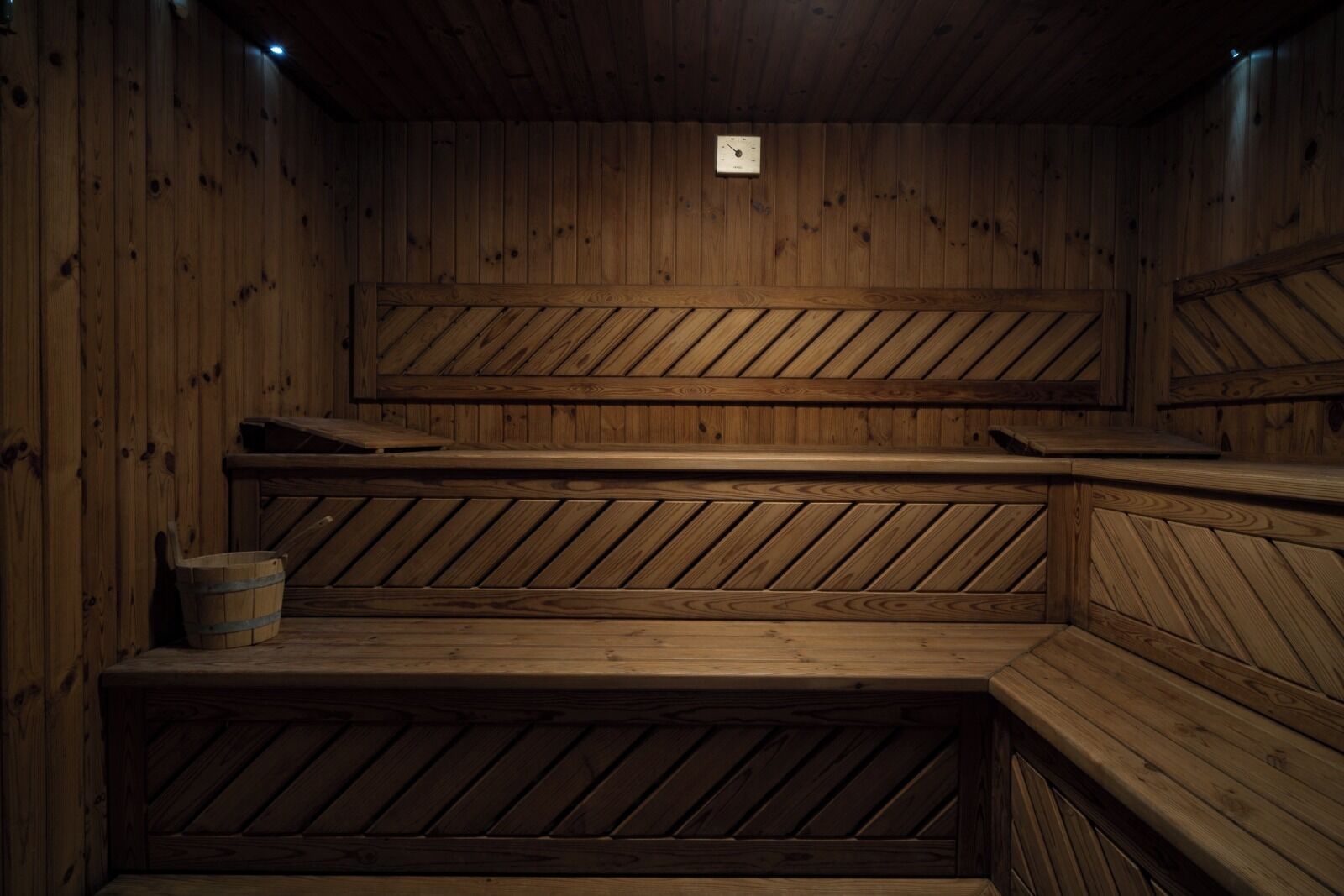 A wooden sauna with multiple benches and a small bucket.