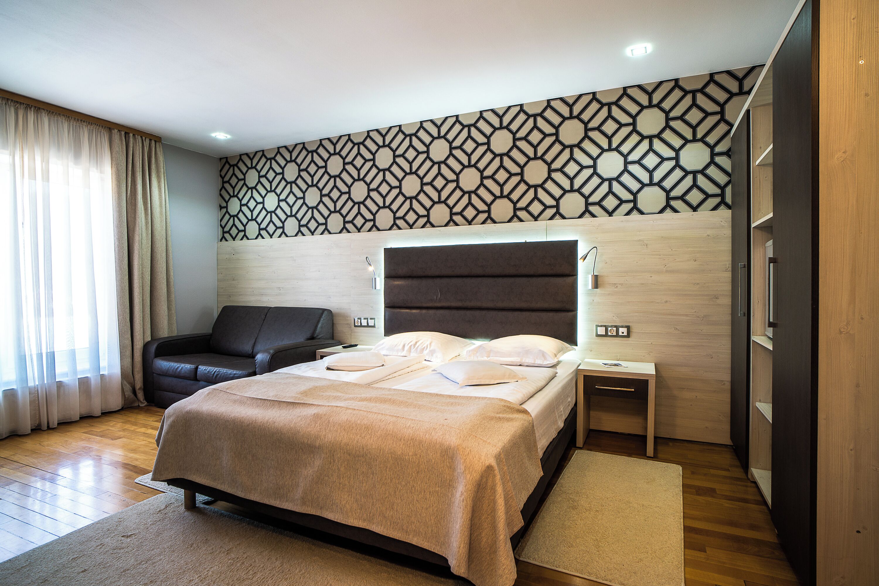A modern bedroom with a large bed, a bedside table, a nightstand, a sofa, and a patterned wall.