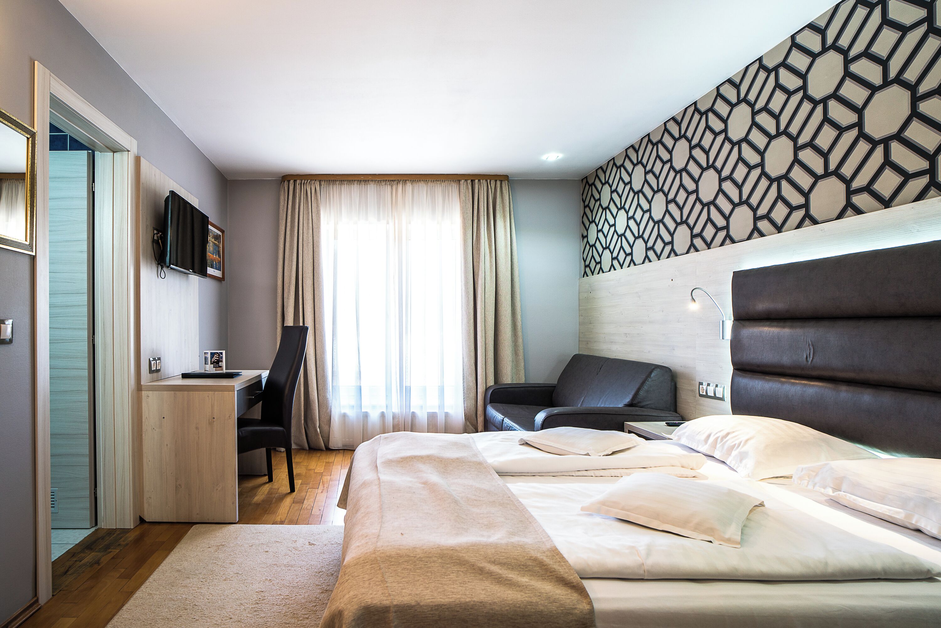 Habitación de hotel con cama, escritorio con silla, televisor montado en la pared y un diseño de pared con motivos.