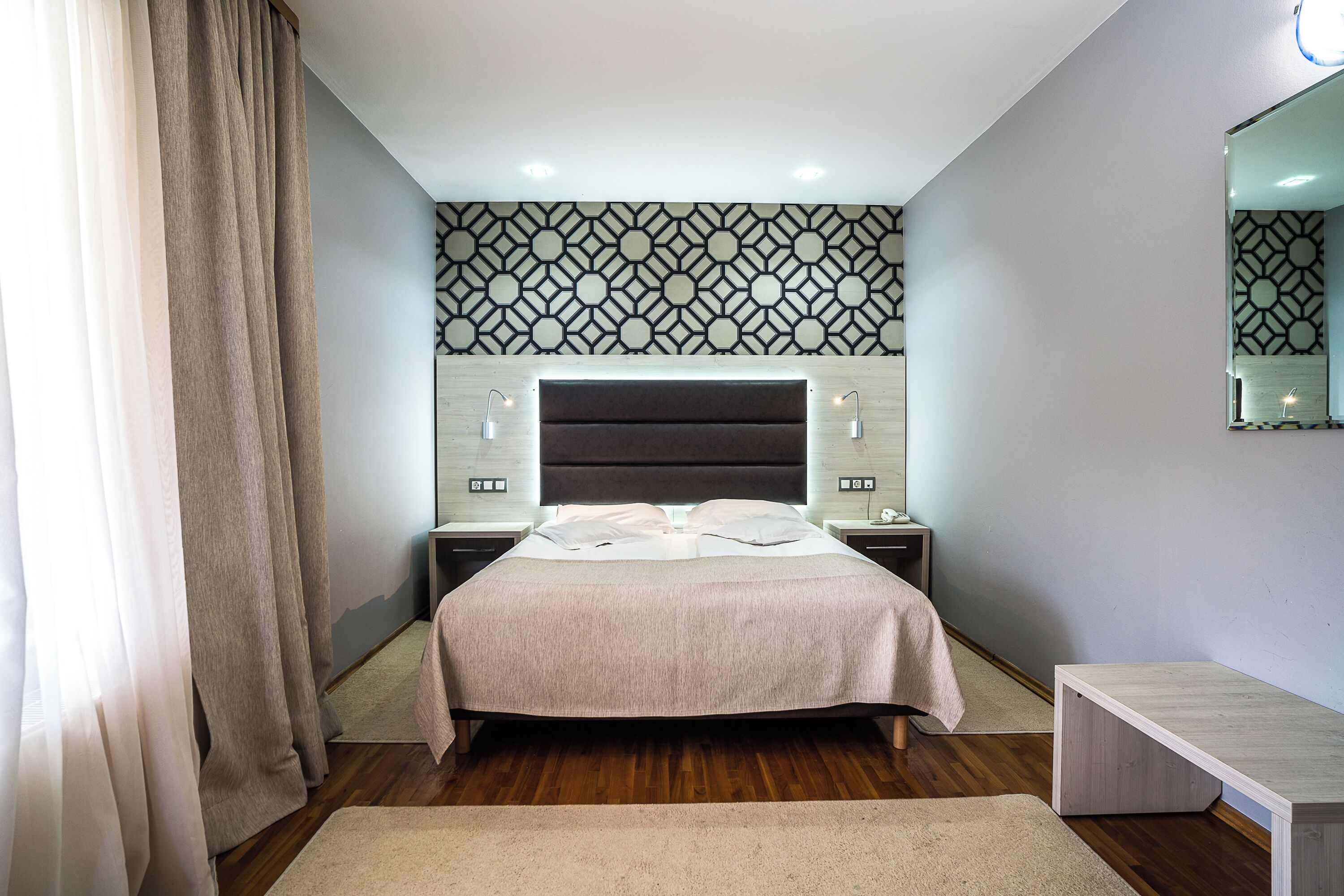 A modern bedroom with a large bed, bedside lamps, a nightstand, a bench, and a patterned wall.