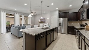 A modern kitchen with dark cabinetry, stainless steel appliances, and pendant lighting. - Spacious/ Near Disney/themed rooms/ private pool & game room/ resort grounds (Kissimmee)