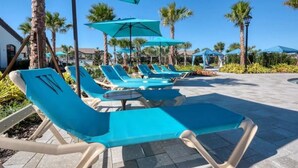 A poolside area with blue lounge chairs and umbrellas, surrounded by palm trees and a clear sky. - Spacious/ Near Disney/themed rooms/ private pool & game room/ resort grounds (Kissimmee)