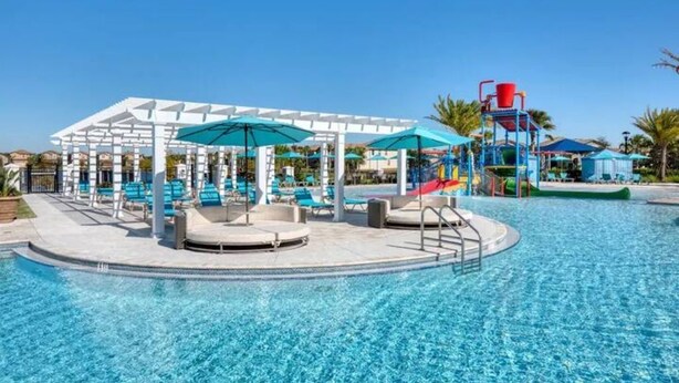 A swimming pool with lounge chairs and umbrellas, a water slide, and a covered area with a white roof. - Spacious/ Near Disney/themed rooms/ private pool & game room/ resort grounds (Kissimmee)