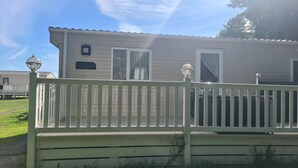 Une maison mobile de plain-pied, à l’extérieur blanc, avec une véranda dotée d’une balustrade blanche et une enseigne indiquant « Summer Breeze Deluxe ».