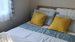 Une chambre à coucher avec un lit, deux oreillers, une fenêtre avec des rideaux et une lampe de chevet.