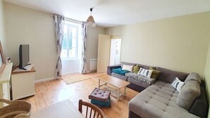 Een woonkamer met een bank, een salontafel, een tv op een dressoir, en een deur naar een andere kamer.