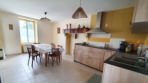 Een keuken met houten kastjes, een eettafel met stoelen en een groot raam.