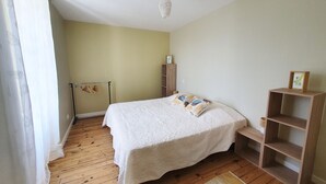 Een slaapkamer met een bed, houten vloer, een houten plank en een kledingrek.