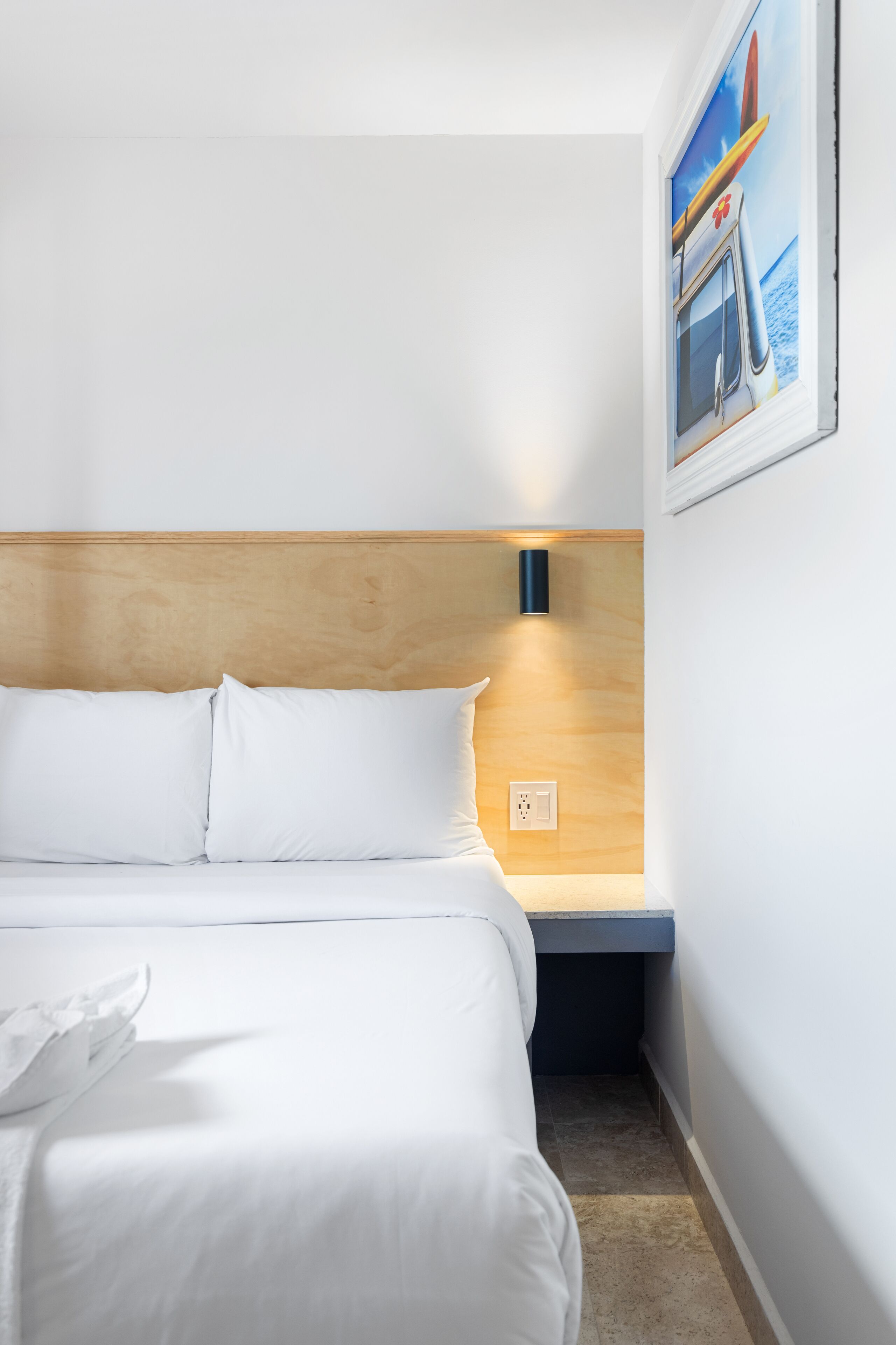 Ein Hotelzimmer mit hölzernem Kopfteil, weißer Bettwäsche, einem kleinen Nachttisch und einer Wandleuchte.