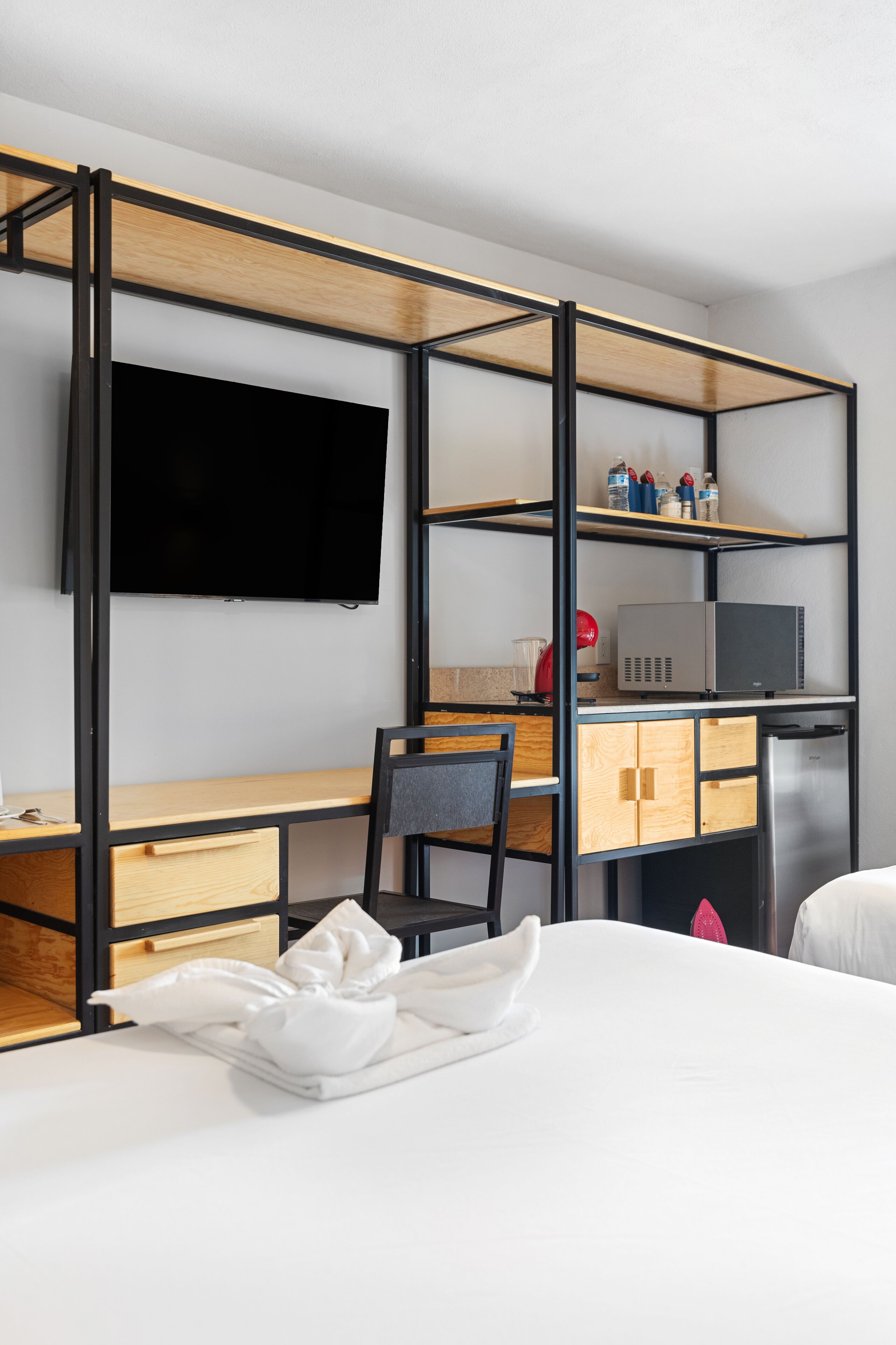 Habitación de hotel con cama, escritorio con silla, televisor montado en la pared y microondas sobre el escritorio.