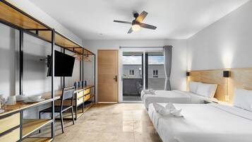 Habitación de hotel moderna con escritorio, dos camas, ventilador de techo y vistas al exterior.