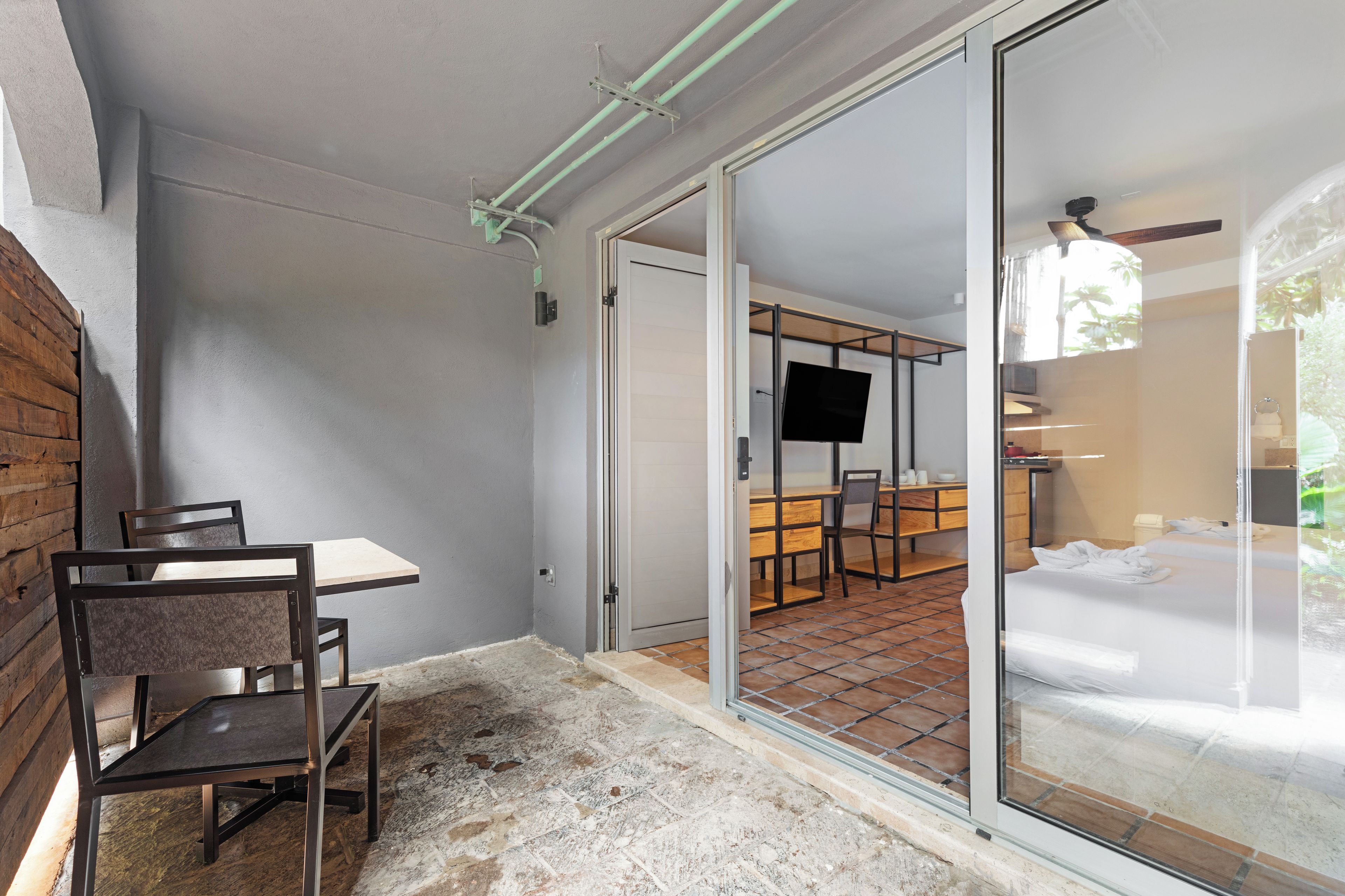 A hotel room with a sliding glass door leading to a balcony, a bed, a desk with a chair, and a television on the wall.