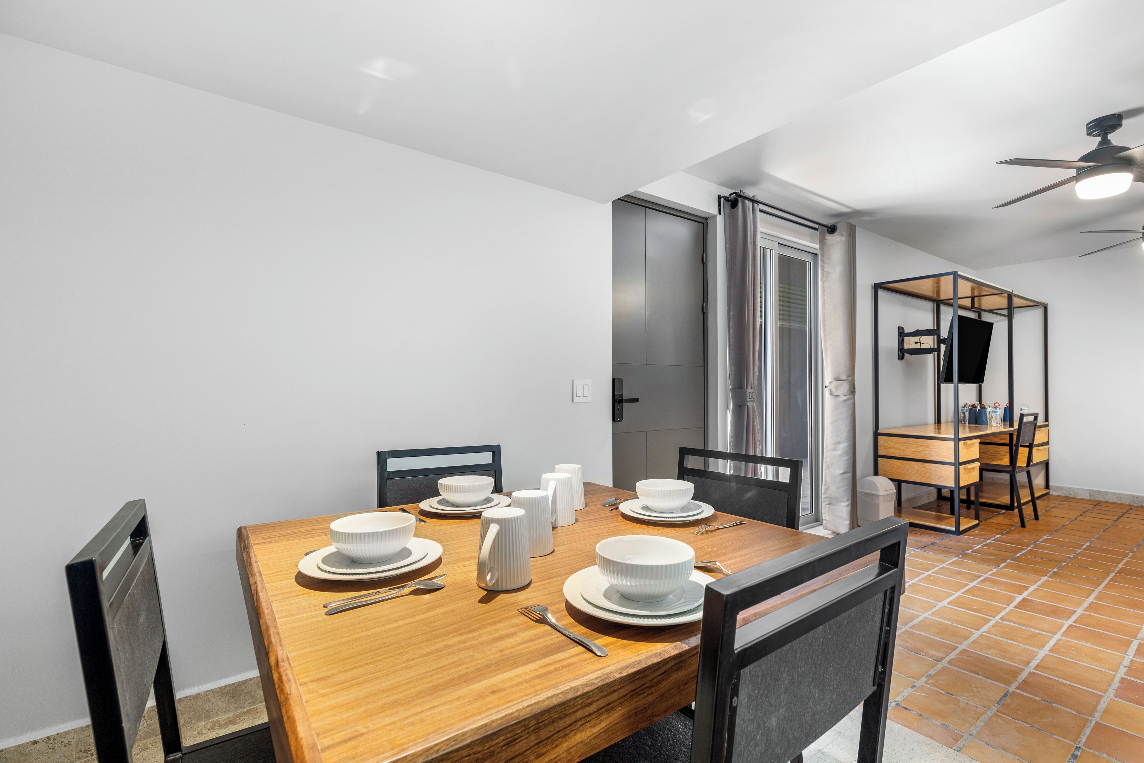 A dining area with a wooden table set for four, chairs, and a small kitchen area with a counter and cabinets.