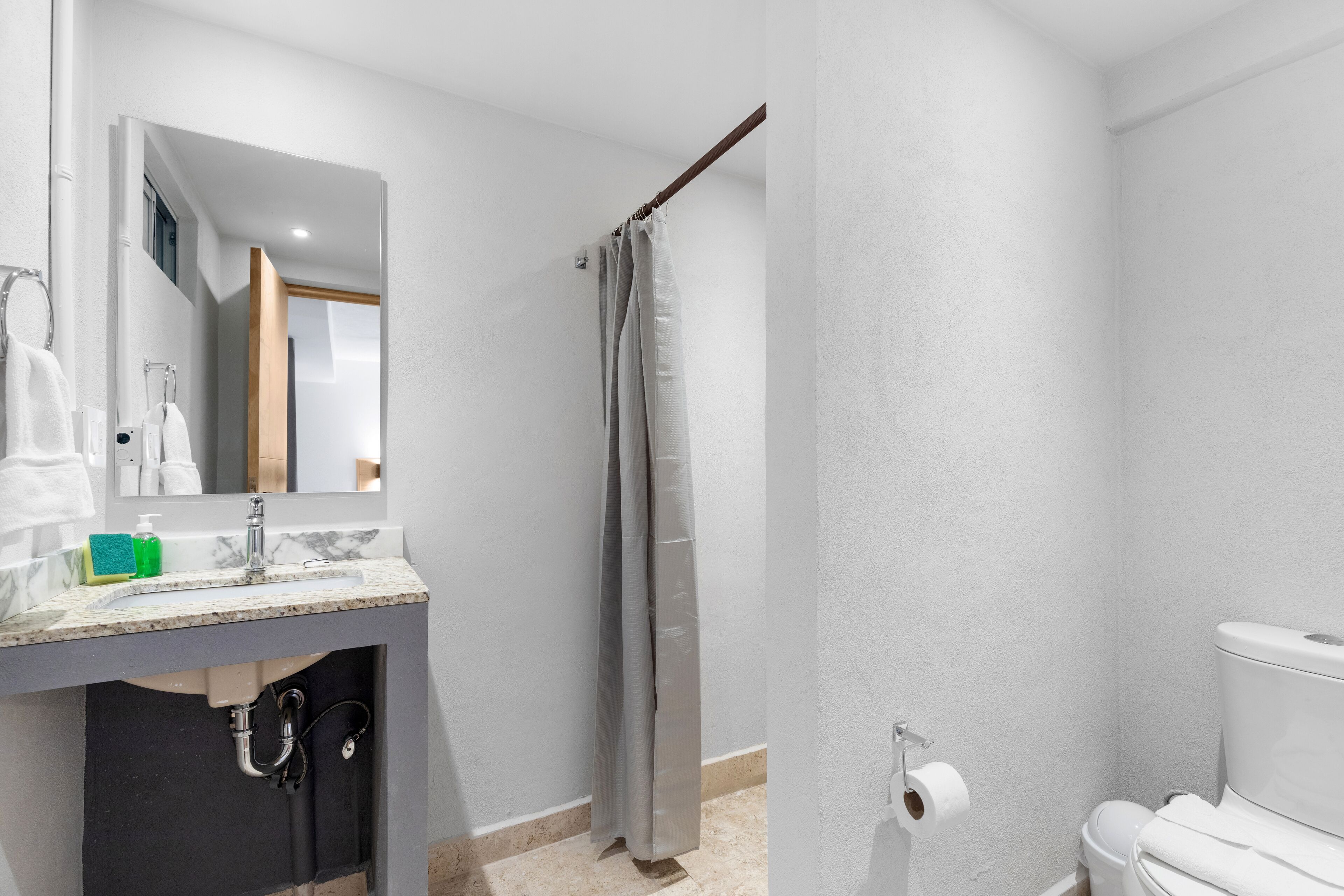 Un baño con lavamanos, espejo, inodoro y cortina de ducha.