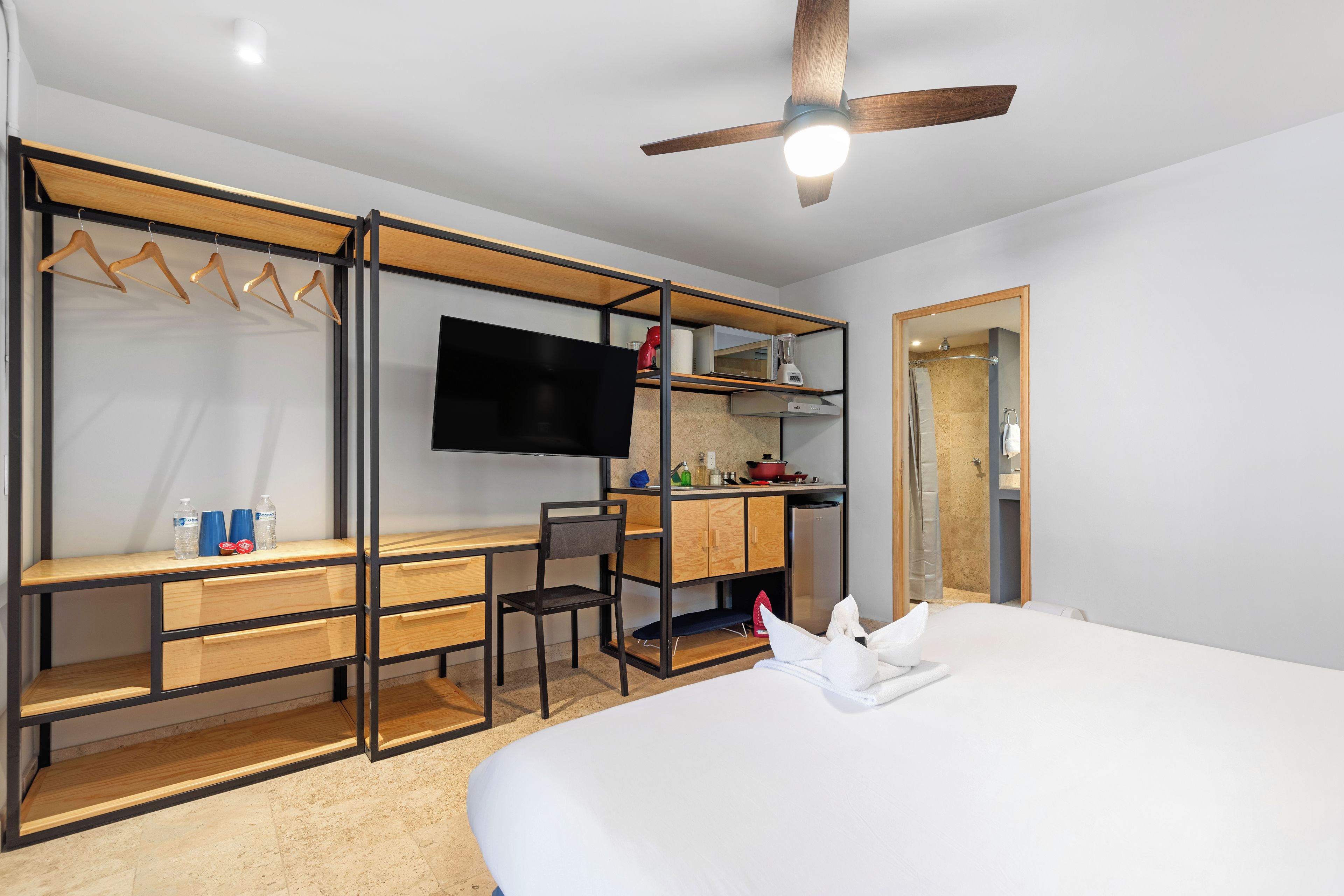 Une chambre d’hôtel moderne équipée d’un lit, d’un bureau, d’une chaise, d’une télévision et d’une kitchenette.