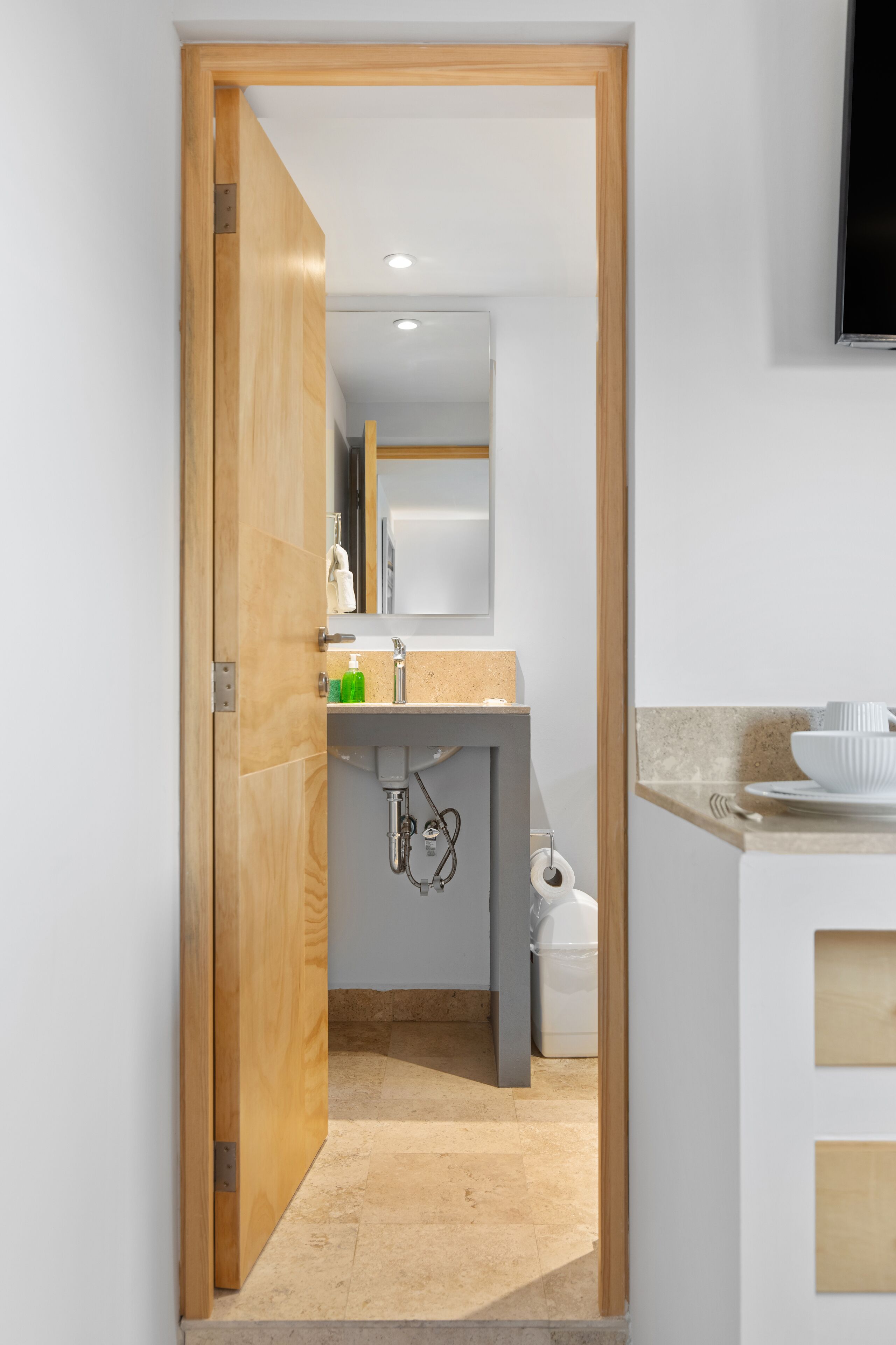 A narrow hallway leading to a bathroom with a wooden door, a sink, and a mirror.