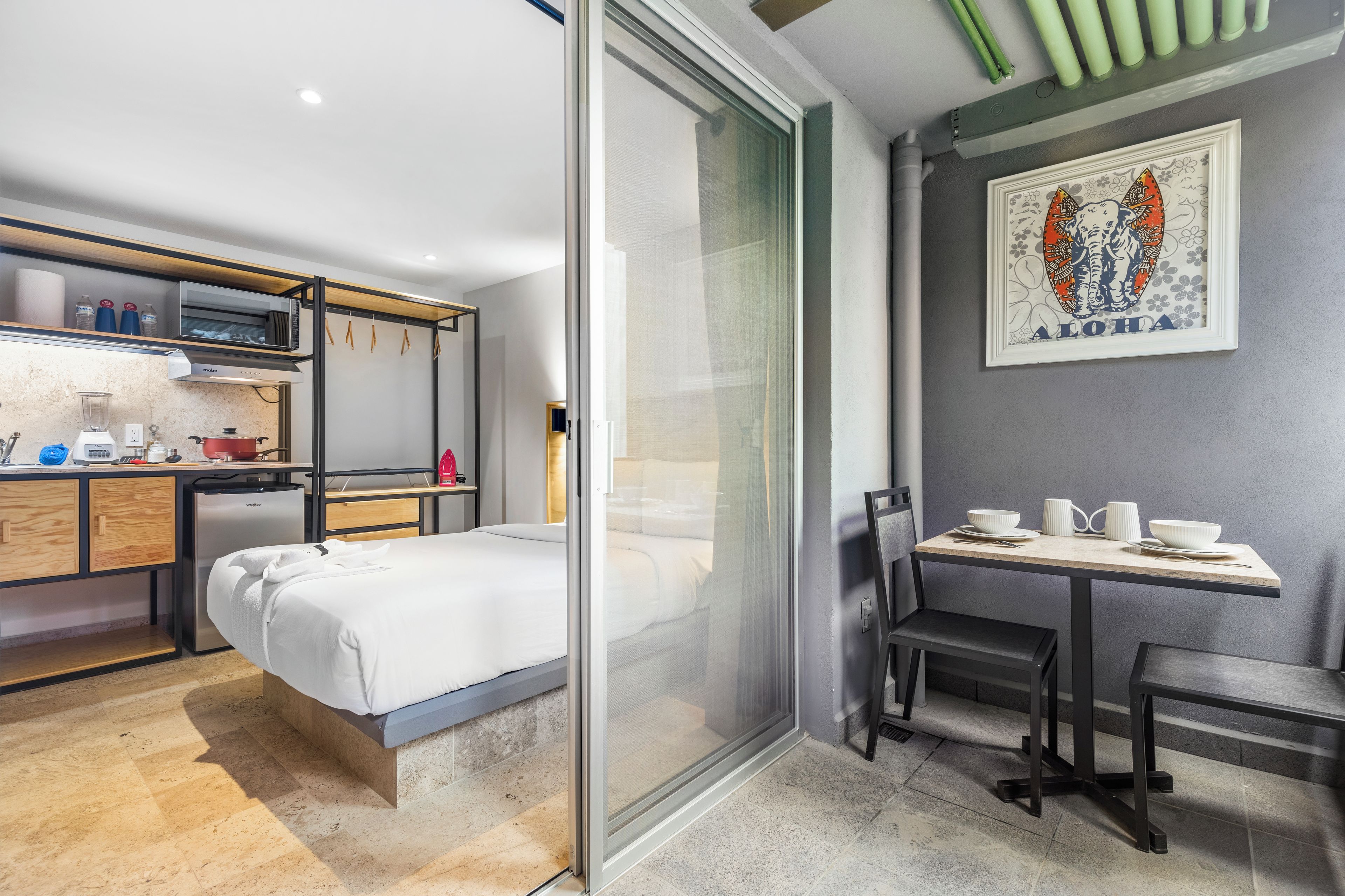 A compact hotel room with a bed, kitchenette, and a dining area with a table and chairs.