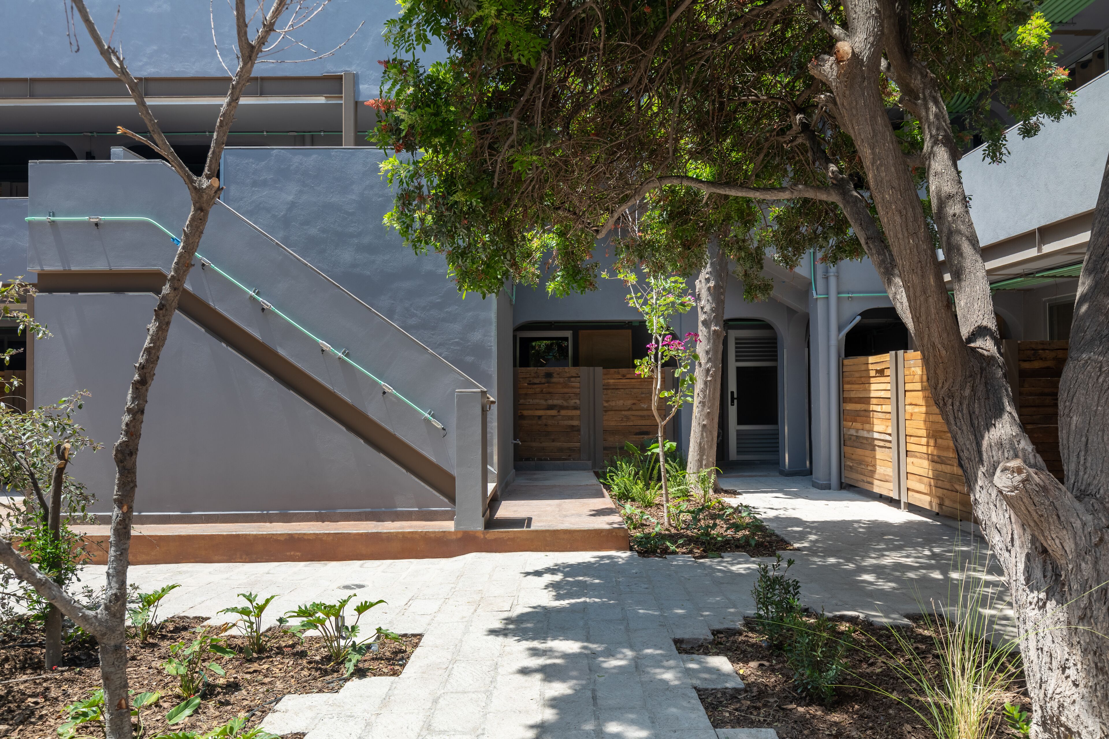 Un edificio moderno con una escalera, una puerta de madera y un jardín con plantas y árboles.