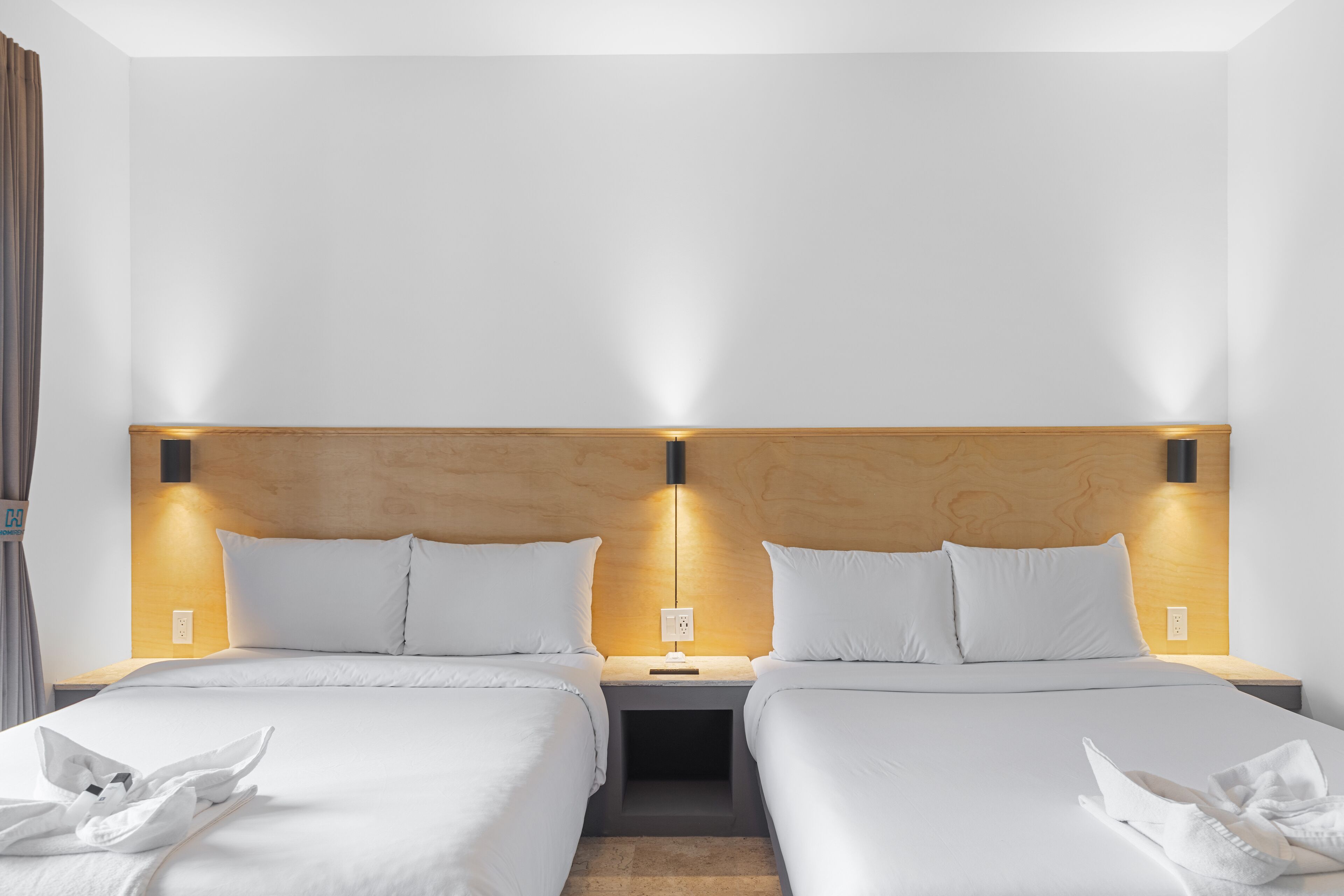 A hotel room with two beds, each with white linens and a wooden headboard. There are bedside tables with lamps and a power outlet on each side.