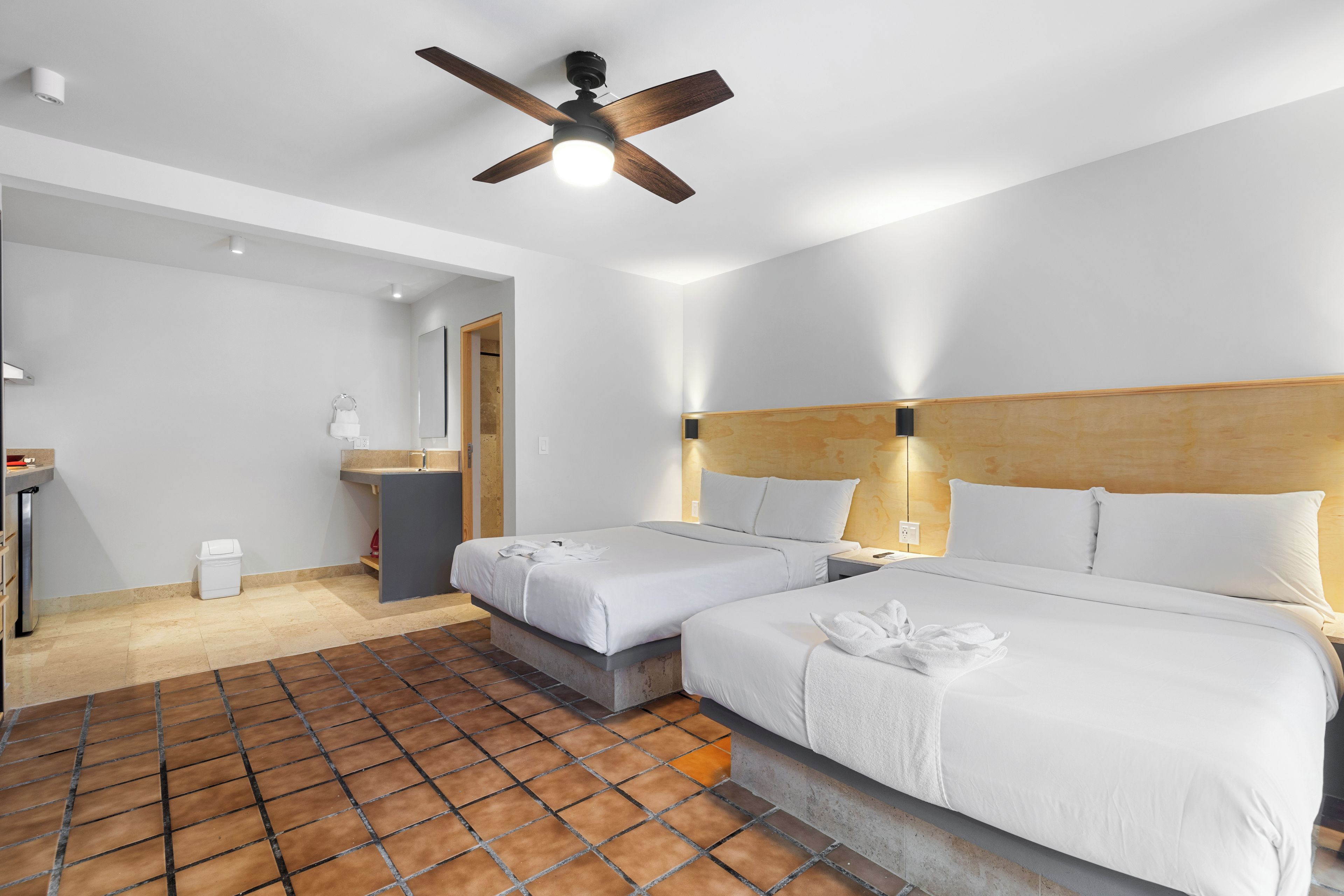 A hotel room with two beds, a ceiling fan, a bathroom, and a tiled floor.