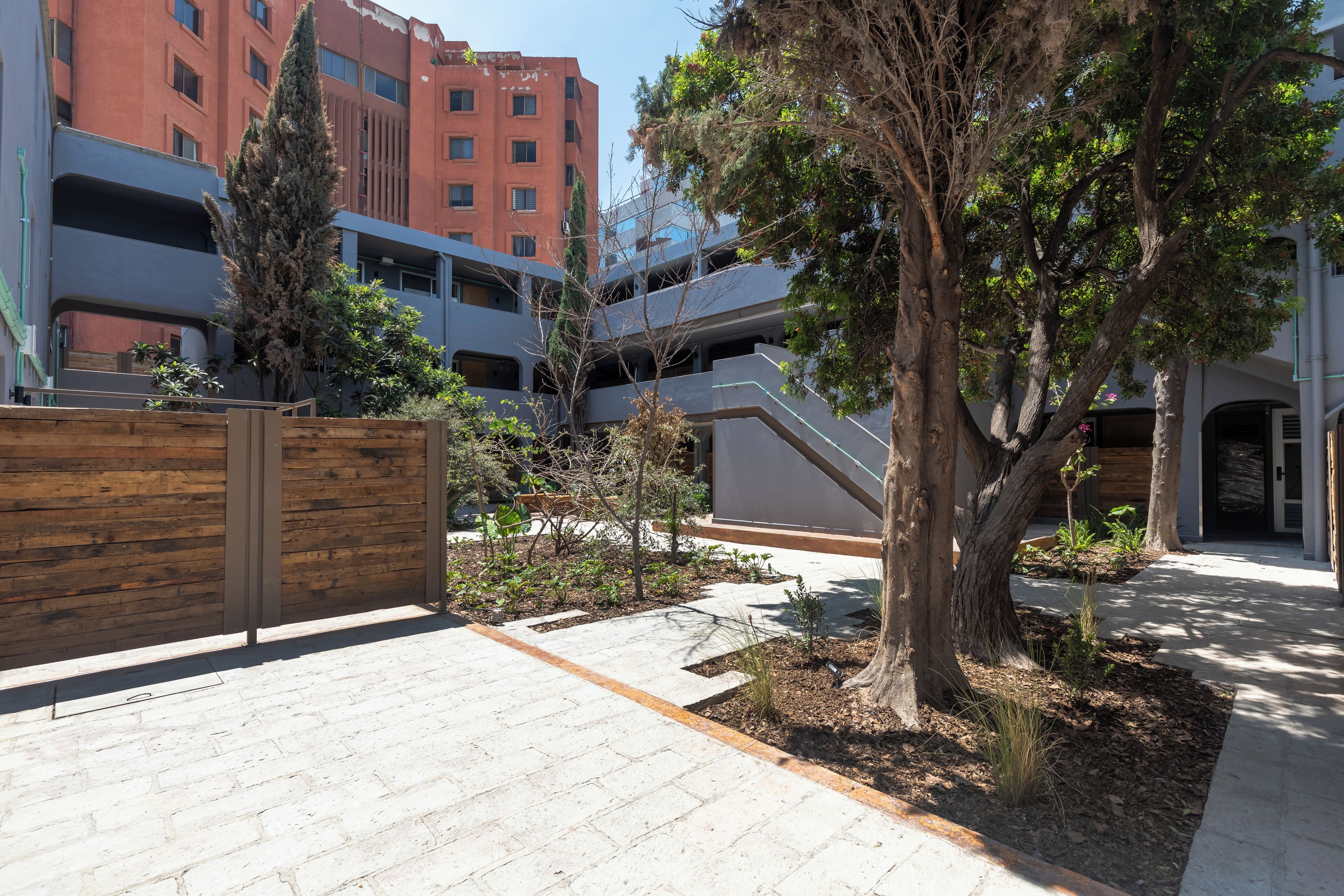 A courtyard with a wooden fence, a tree, and a building with multiple balconies.