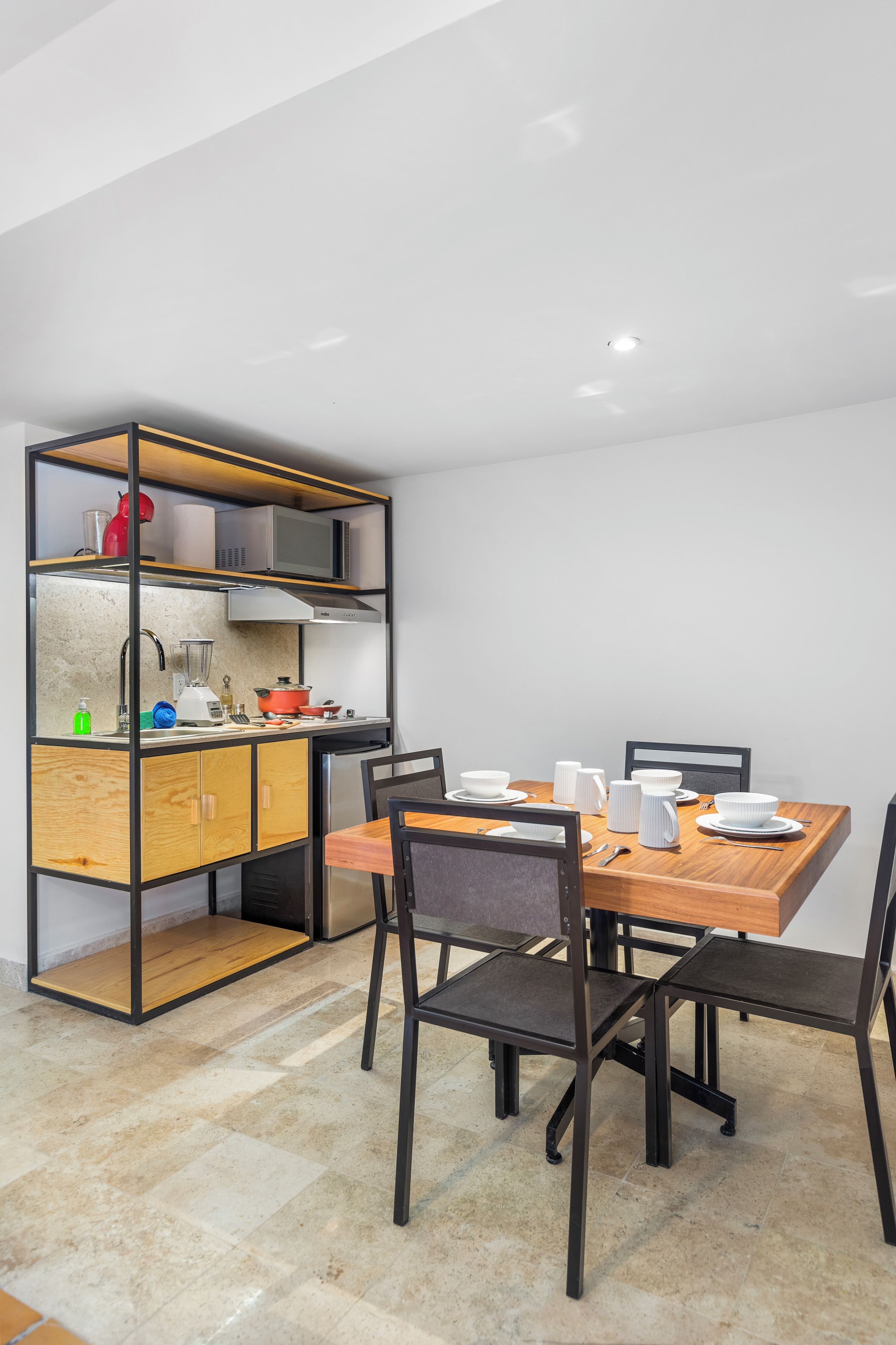A modern kitchen with a built-in microwave, a stove, and a sink. There is a dining table with chairs and a small kitchen island with a microwave and a red kettle.