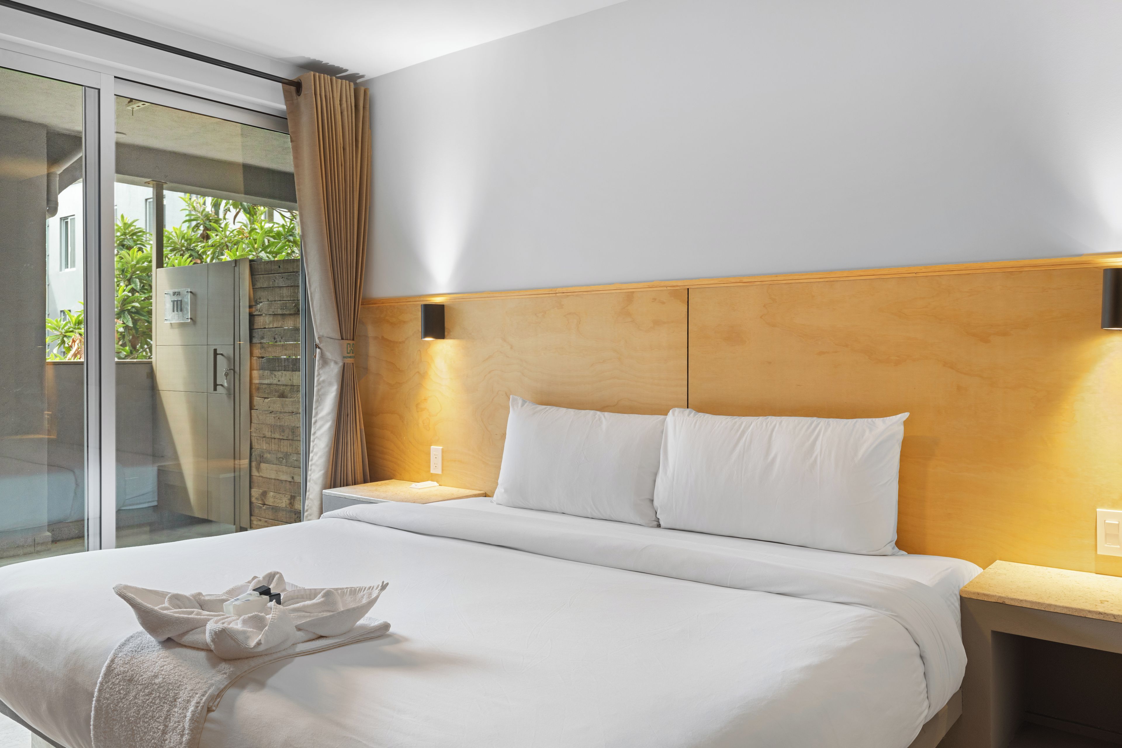 A hotel room with a large bed, a glass door leading to a balcony, and a wooden headboard.