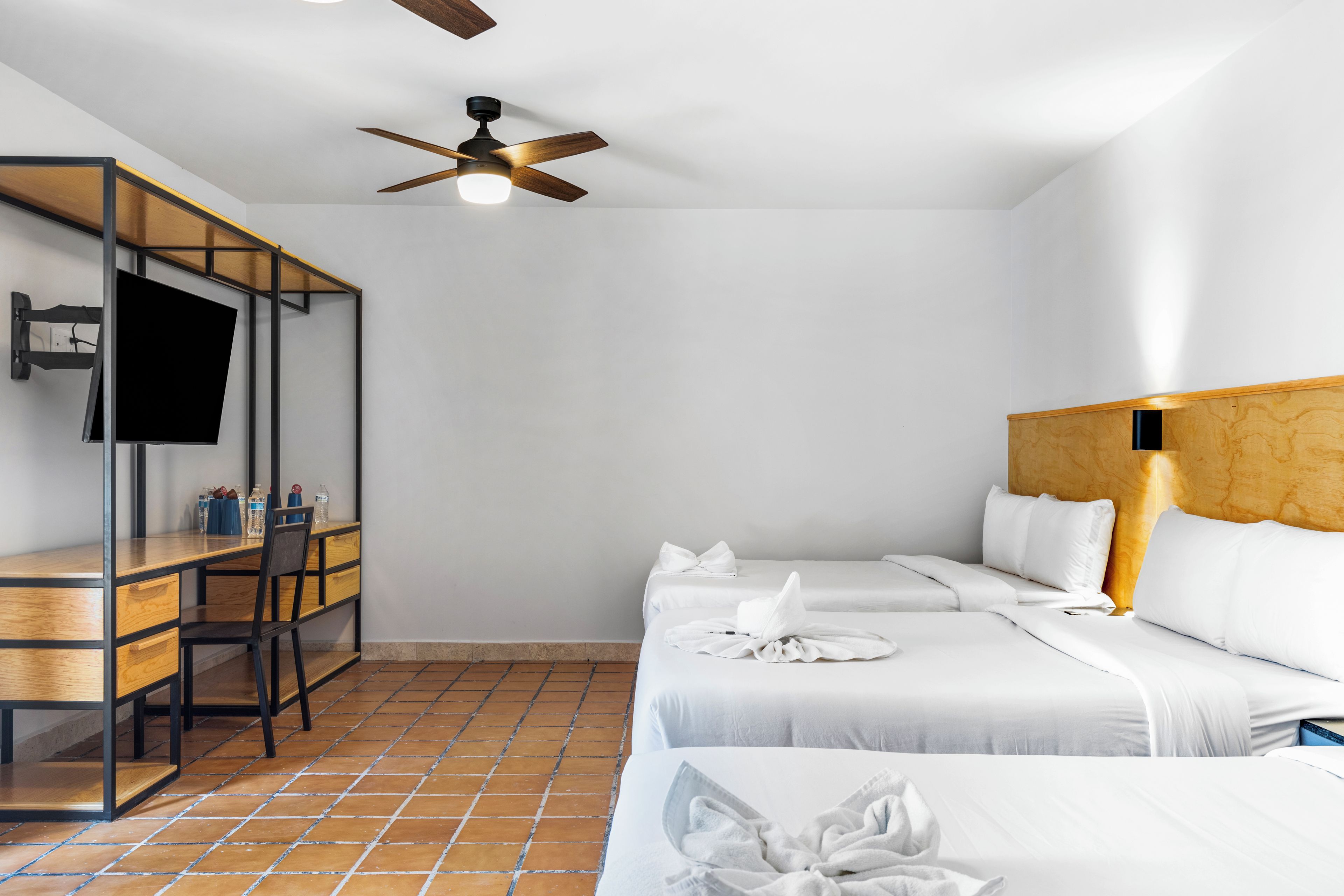 A hotel room with a bed, a desk, a chair, a TV, and a ceiling fan.