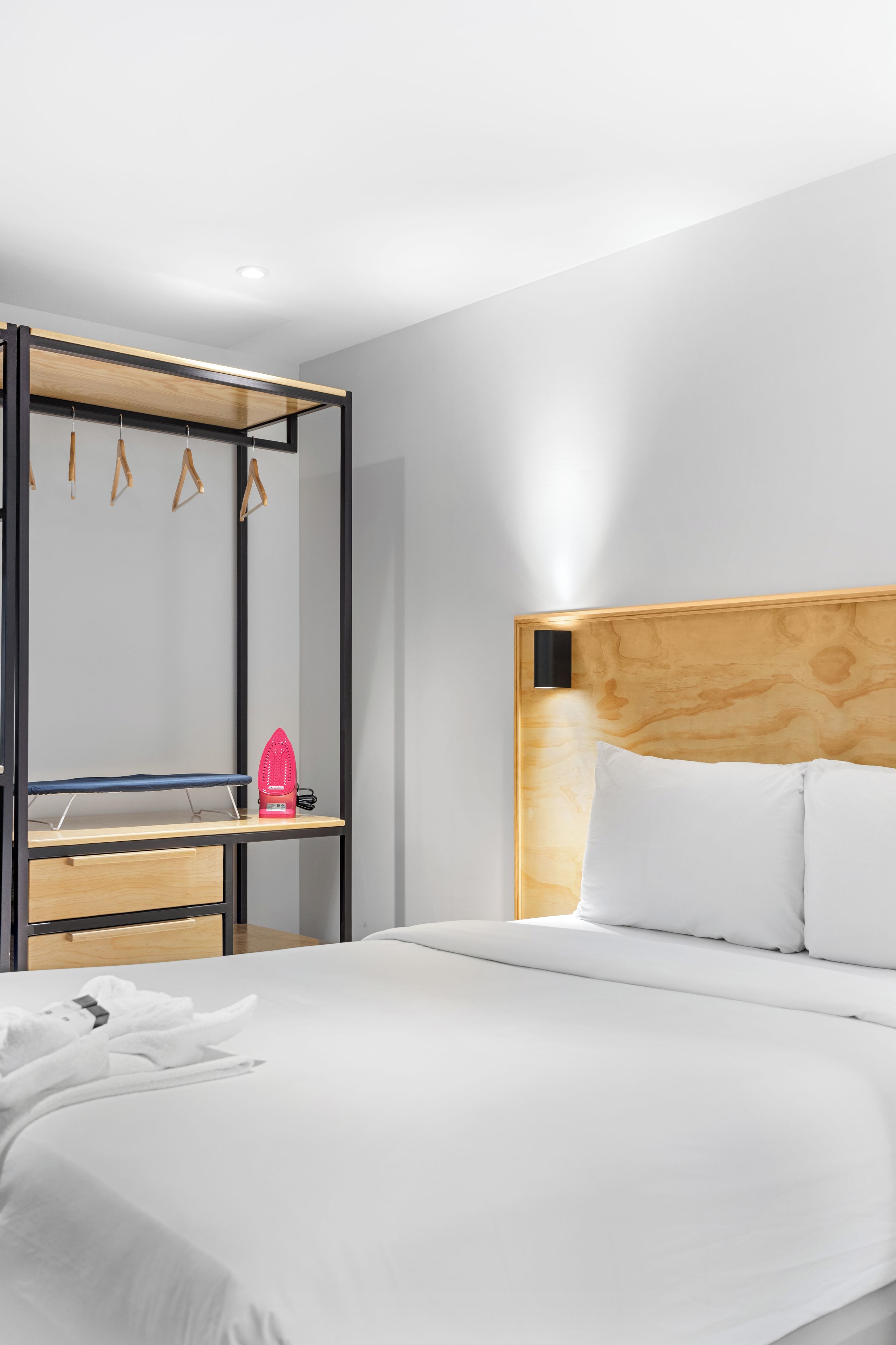 Habitación de hotel con cama, cabecero de madera, armario con espejo y perchero.