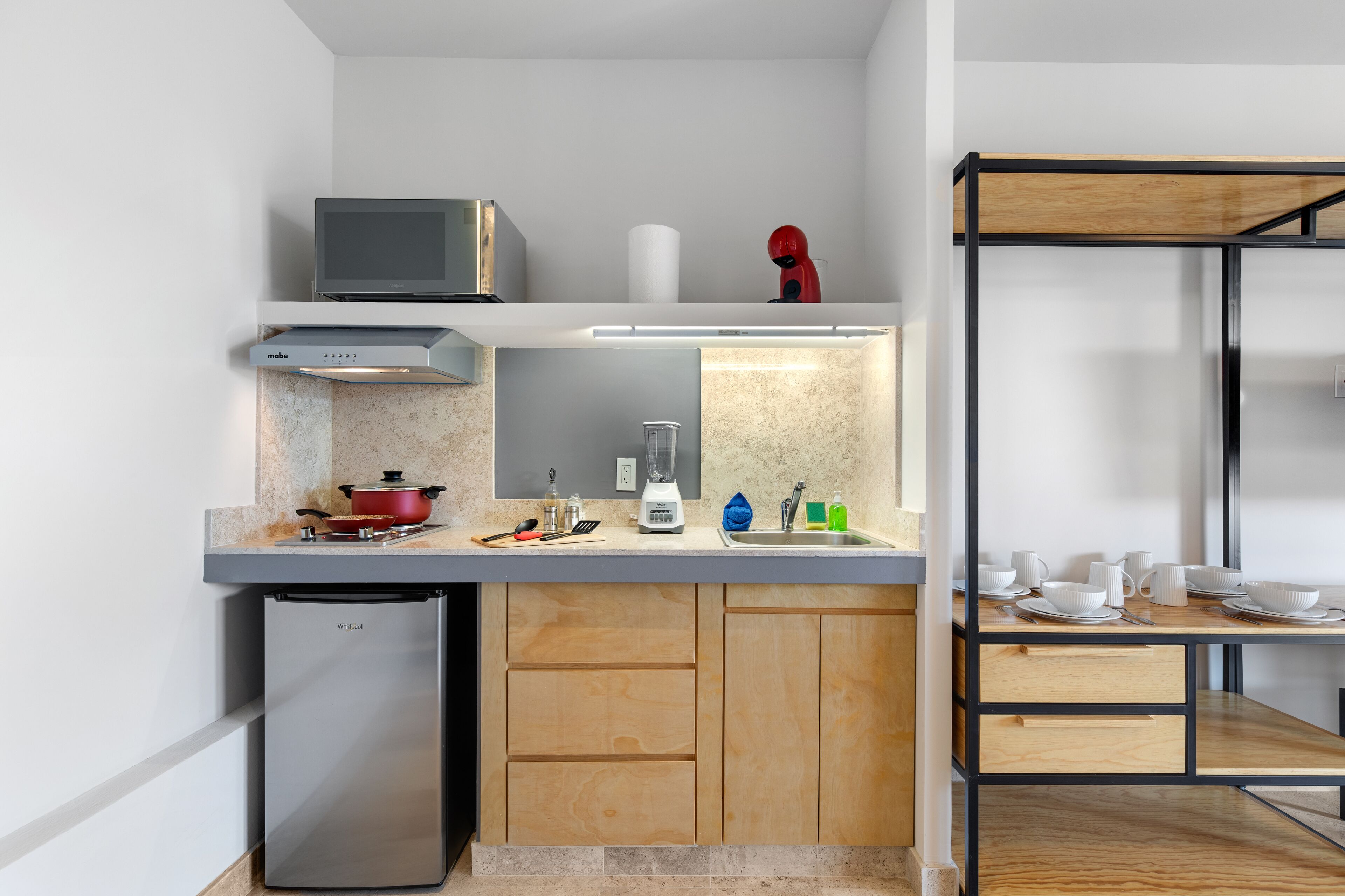 Una cocina compacta con microondas integrado, un refrigerador pequeño y una encimera de madera.