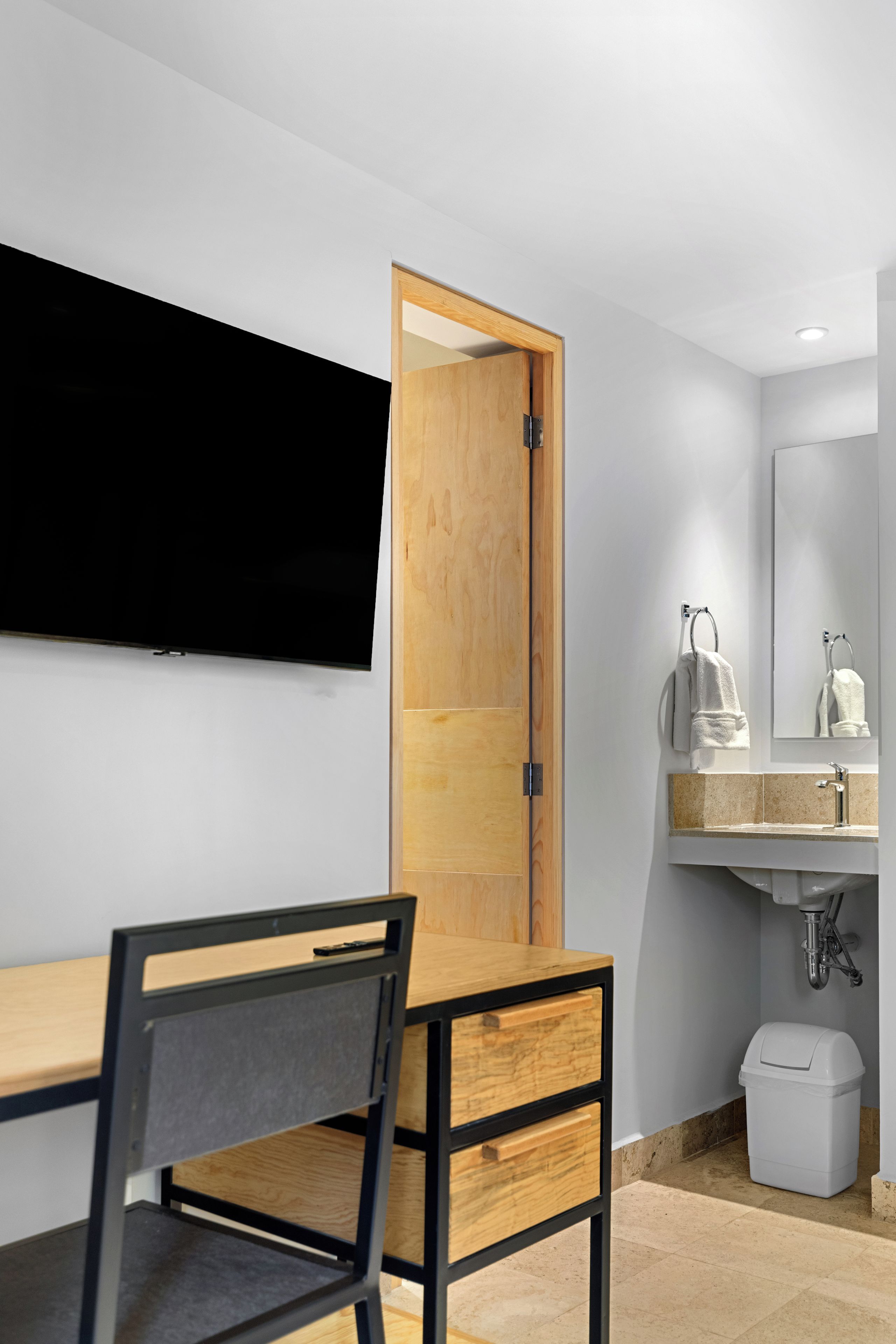 Un baño moderno con puerta de madera, un lavamanos con espejo y un inodoro.