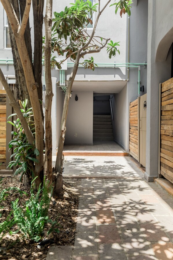 A narrow pathway leading to a staircase in a building with a modern design, surrounded by trees and a wooden fence. - Hacienda Santa Barbara (Querétaro)