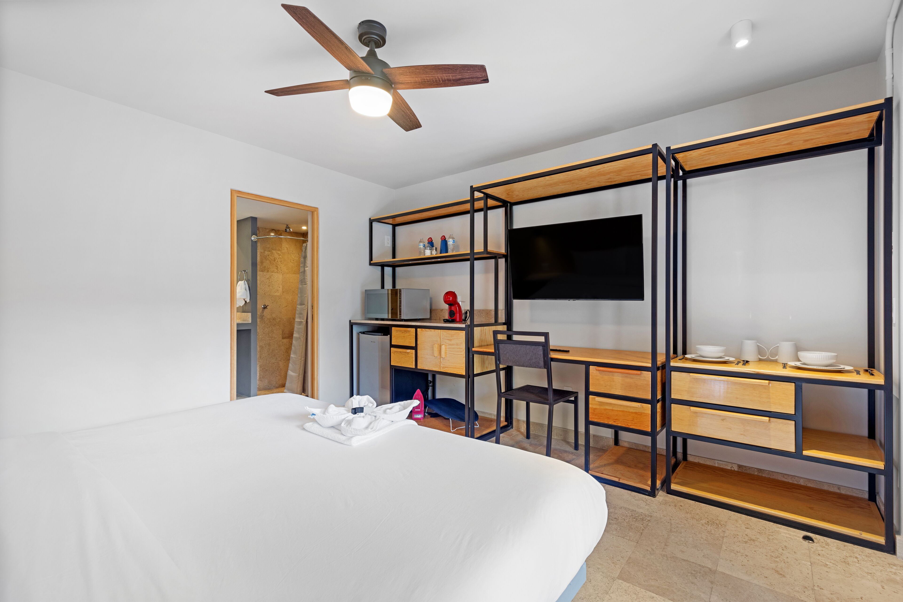 Una habitación de hotel moderna con una cama grande, un escritorio con silla, un televisor y un armario con estantes.