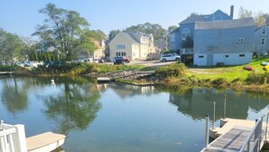 A calm lake with a dock and a small boat, surrounded by grassy areas and houses.