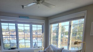 A living room with a sofa, armchair, coffee table, and a view of a body of water through large windows.