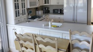 A kitchen with white cabinetry, a chandelier, a refrigerator, and a dining area with wooden chairs and a table.