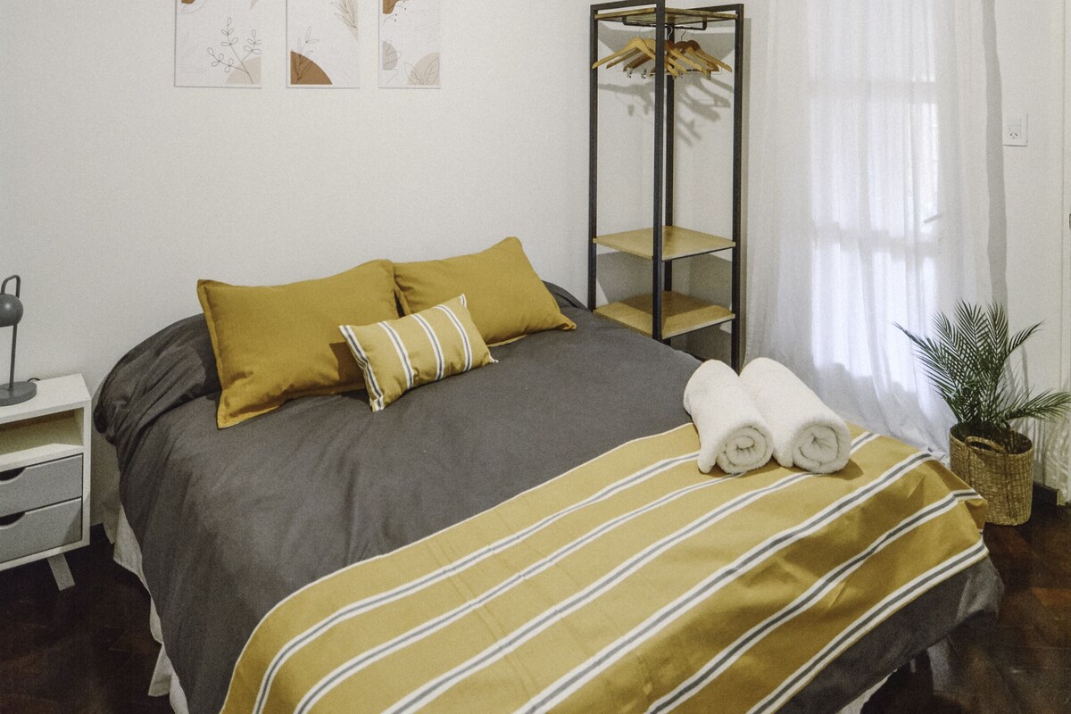 Een keurig opgemaakt slaapkamer met een bed, nachtkastje en een hangende lamp.