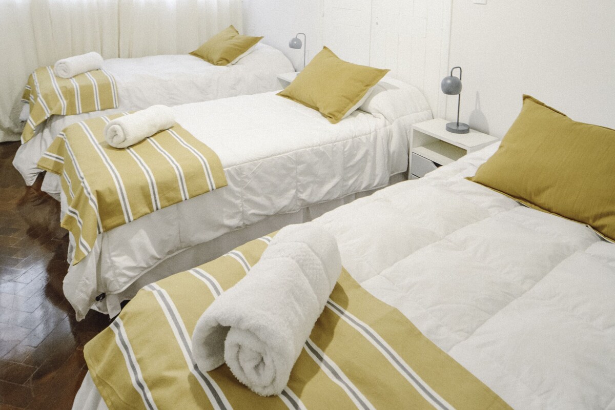 Een hotelkamer met twee bedden, elk voorzien van gestreept beddengoed en kussens, een nachtkastje met een lamp, en een hangende lamp.