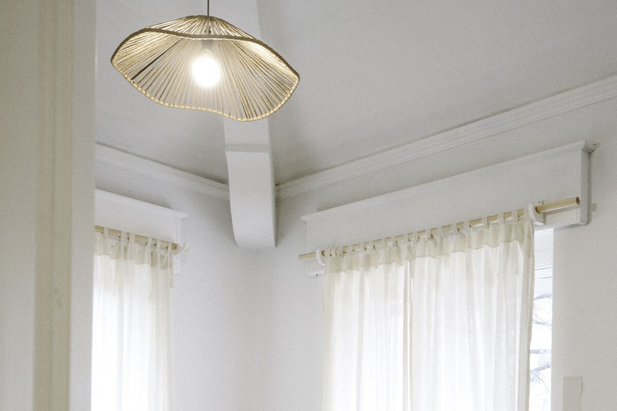 Een slaapkamer met een bed, gordijnen, een hanglamp en een raam.