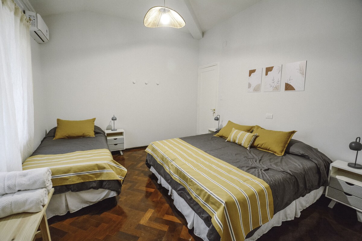 Een hotelkamer met twee bedden, een houten vloer, een witte muur en een plafondventilator.