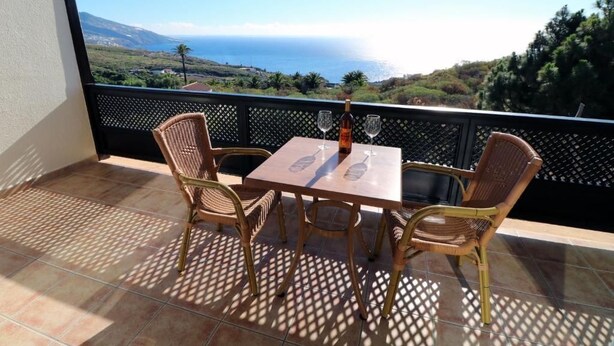 Un balcón con mesa y sillas, con vistas panorámicas al mar y las colinas.