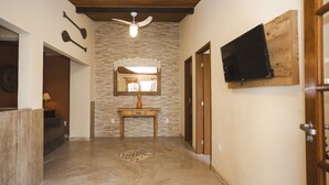 A hallway with a wooden ceiling, a ceiling fan, a stone wall, a wooden console table, a television mounted on a wooden board, and a patterned rug on the floor. - R. Virgínia 48 (Búzios)