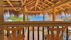 Eine Holzterrasse mit einem Reetdach, das auf einen Strand blickt.