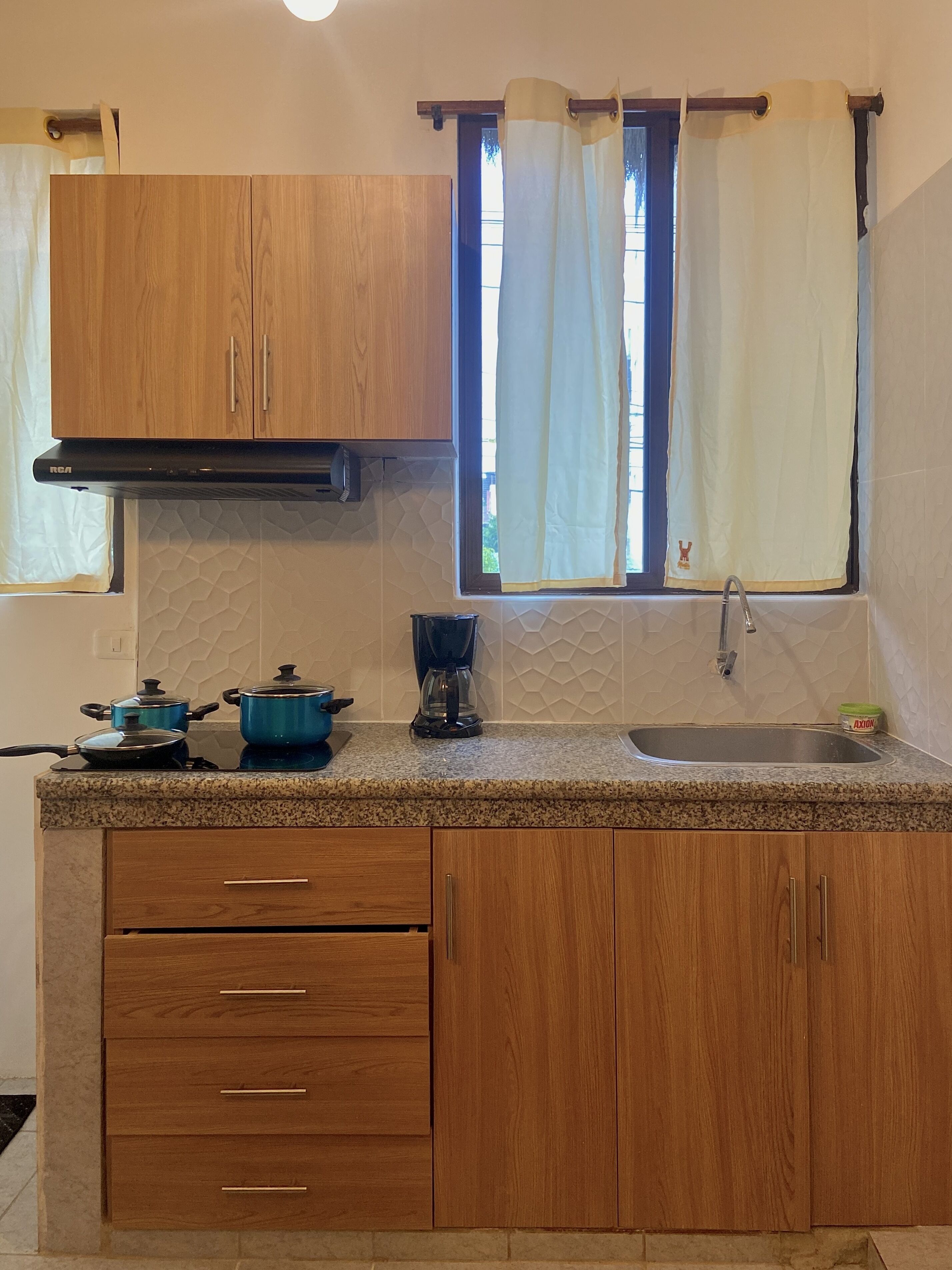 A kitchen with wooden cabinets, a granite countertop, a coffee maker, and a window with curtains.